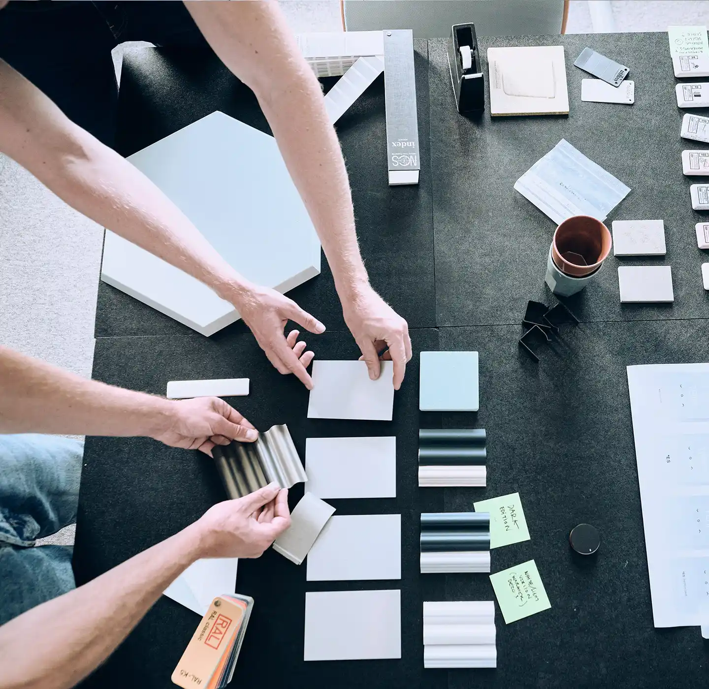 Hands arranging color swatches and material samples on a table during a design planning session.