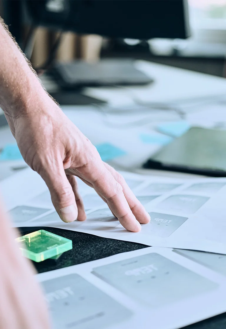 Hand pointing at papers with design sketches on a desk.