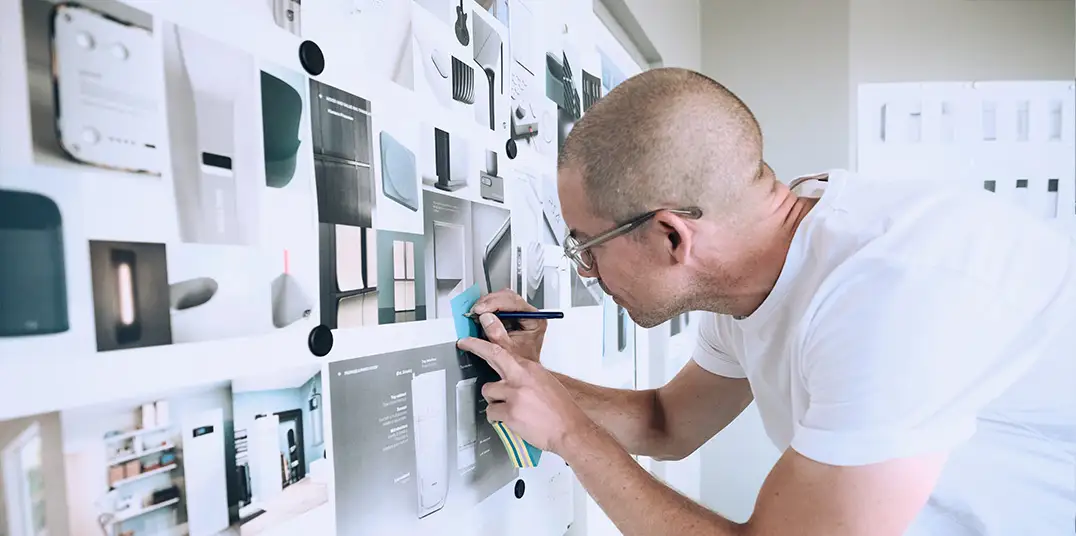 Designer adding notes to a wall of product sketches and concept images during the heat pump design process.