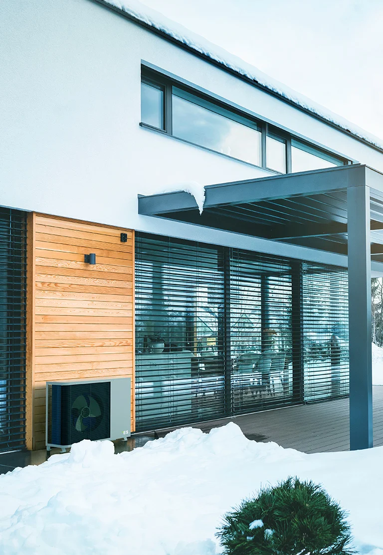 Modern house with large windows, snow-covered terrace and an energy-efficient heat pump.